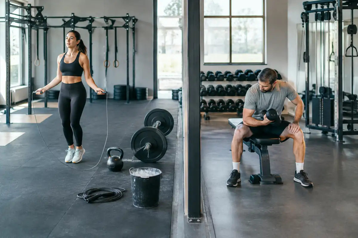 Équipement de CrossFit avec corde et kettlebell face à des haltères et un banc de musculation dans une salle de sport.