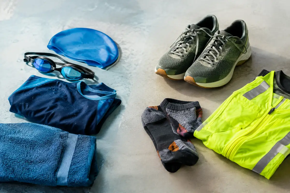 Lunettes et bonnet de natation posés à côté de chaussures de course et d’une tenue réfléchissante sur un fond neutre.
