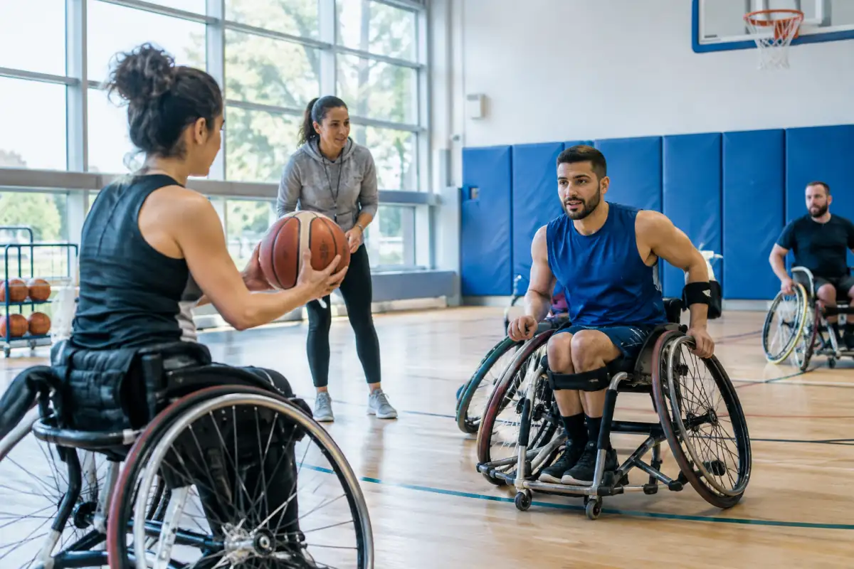 Séance de basket fauteuil dans un gymnase accessible, avec un encadrant et du matériel adapté à la pratique sportive.