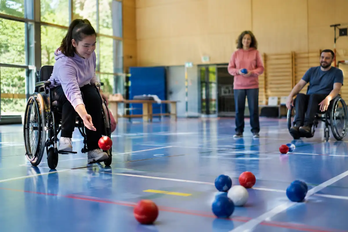 Terrain de boccia aménagé dans une salle accessible, avec des balles colorées et un fauteuil roulant près de l’aire de jeu.