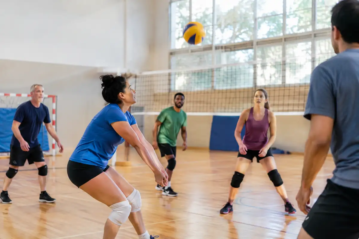 Adultes de niveaux variés se coordonnent autour d’un ballon dans un gymnase, illustration d’un sport en équipe.