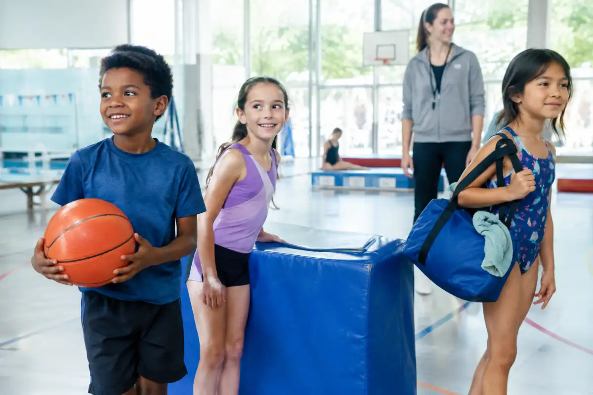 Des enfants découvrent plusieurs activités sportives dans un gymnase lumineux, avec un encadrant attentif en arrière-plan.