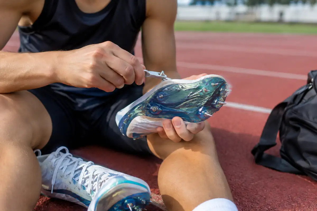 Une athlète vérifie et serre les crampons amovibles de ses chaussures de sprint sur une piste synthétique avant une séance de 100 mètres.