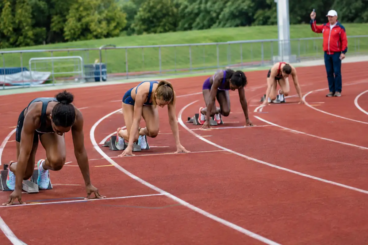Départ d’un 400 mètres en couloirs décalés : les coureurs sont en starting-blocks sous le contrôle du starter.