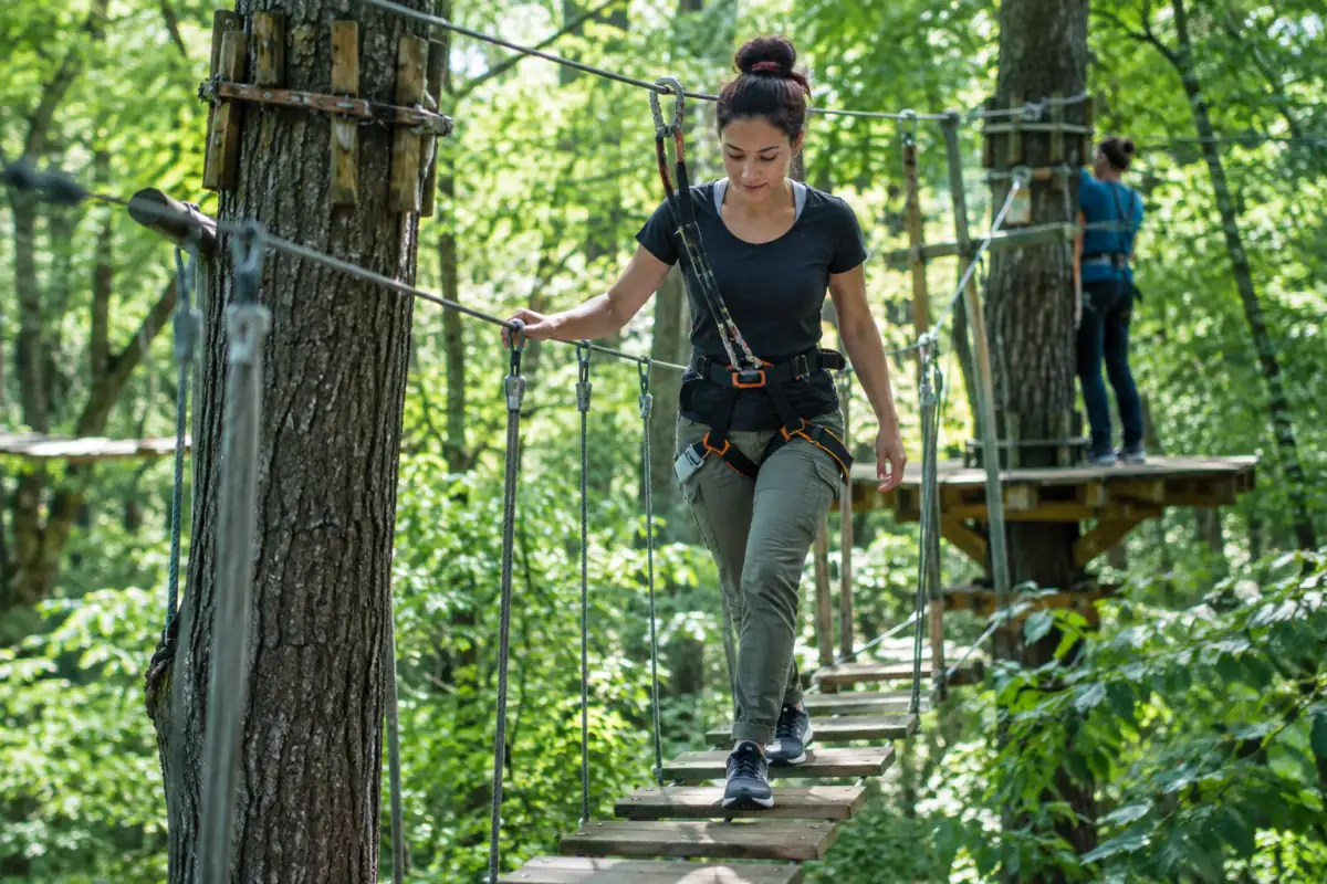 Une participante franchit une passerelle suspendue en accrobranche, équipée d’un baudrier et reliée à la ligne de sécurité.