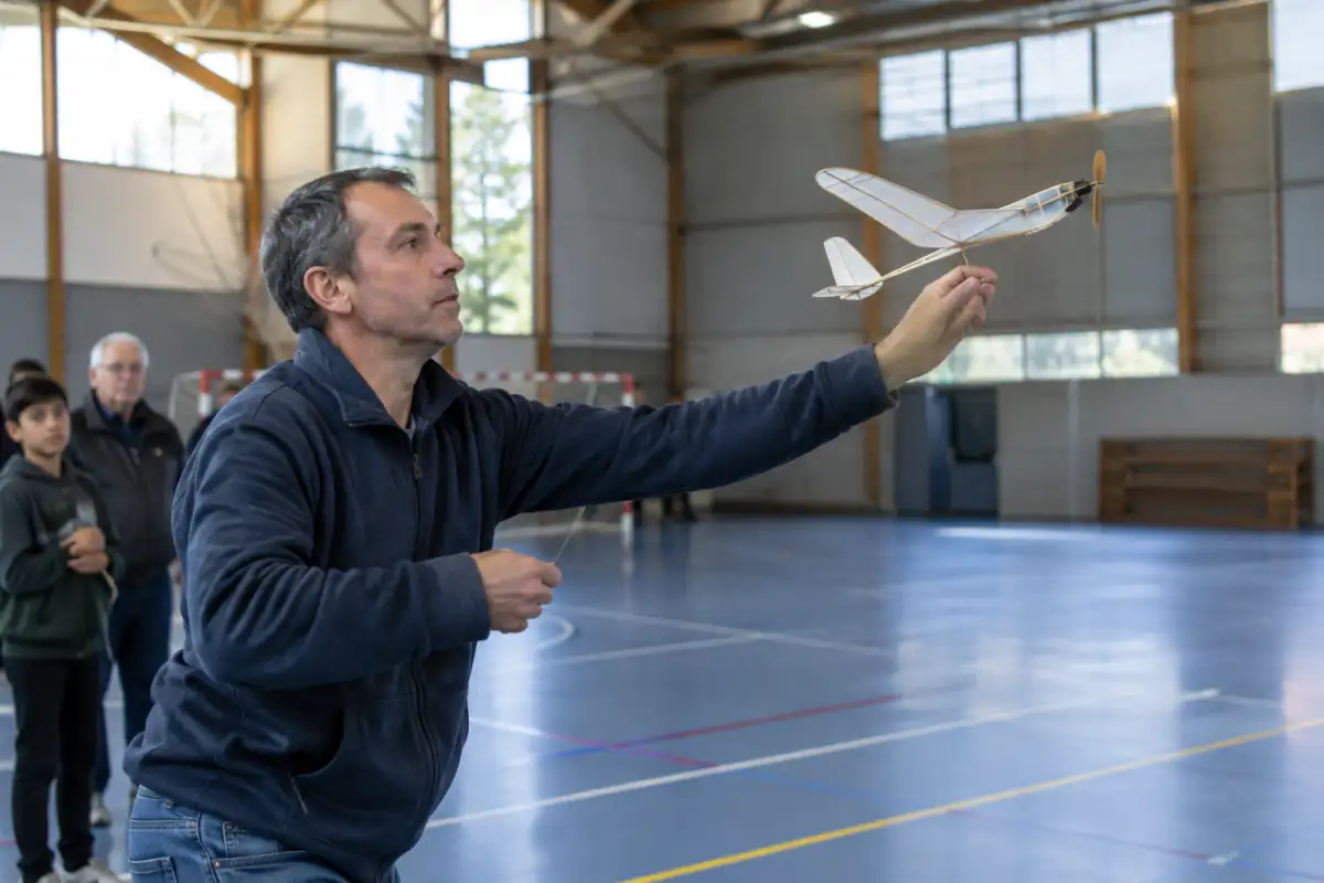 Un pratiquant lance un avion miniature en balsa lors d’une séance d’aéromodélisme en salle dans un grand gymnase.