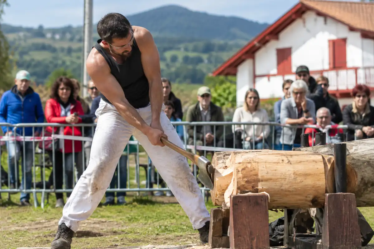 Un aizkolari débite un tronc de hêtre à la hache sur des supports lors d’une épreuve traditionnelle basque en extérieur.
