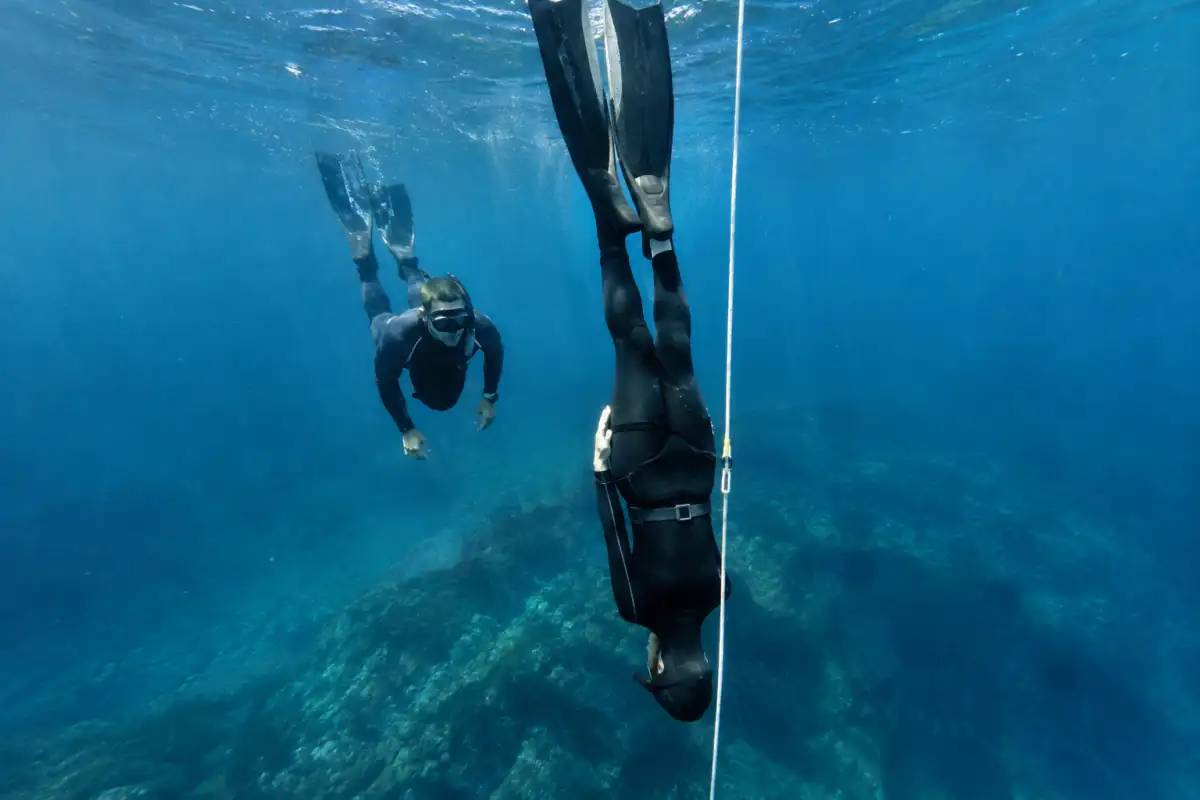 Apnéiste en combinaison et longues palmes descend le long d’une ligne en Méditerranée, surveillé par un binôme de sécurité.