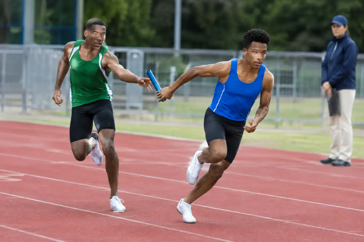 Passage de témoin entre deux relayeurs dans leur couloir, au cœur de la zone réglementaire d’un 4 × 100 m.