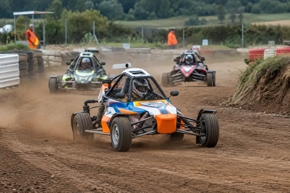 Des buggies d’autocross s’affrontent sur un circuit de terre français, un pilote maîtrisant une glisse en virage.