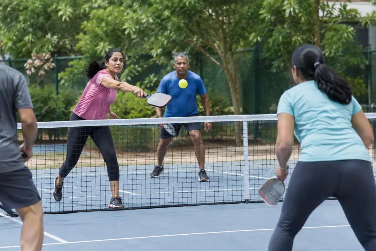 Échange de ball badminton en plein air : un joueur frappe une balle jaune en laine au-dessus du filet.