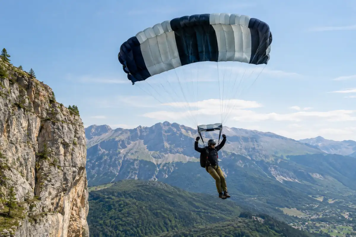 Un pratiquant expérimenté de base jump descend sous sa voile ouverte devant une falaise alpine.