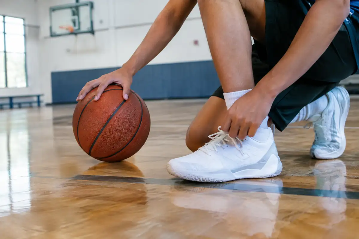 Chaussures de basketball à semelle propre et ballon posés au bord d’un terrain de gymnase pour un débutant en club.