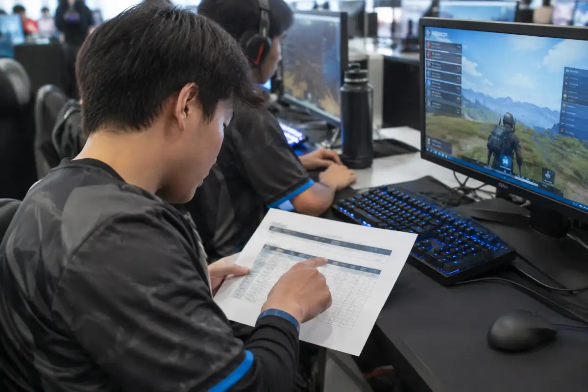 Un joueur vérifie le barème et les consignes d’un tournoi battle royale sur un document posé près de son poste de jeu.