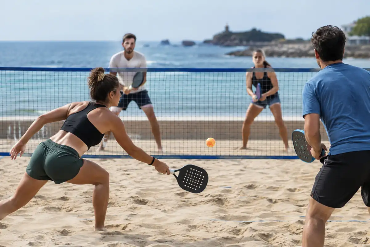 Échange de beach tennis en double sur le sable : une joueuse frappe une balle en volée au-dessus du filet.