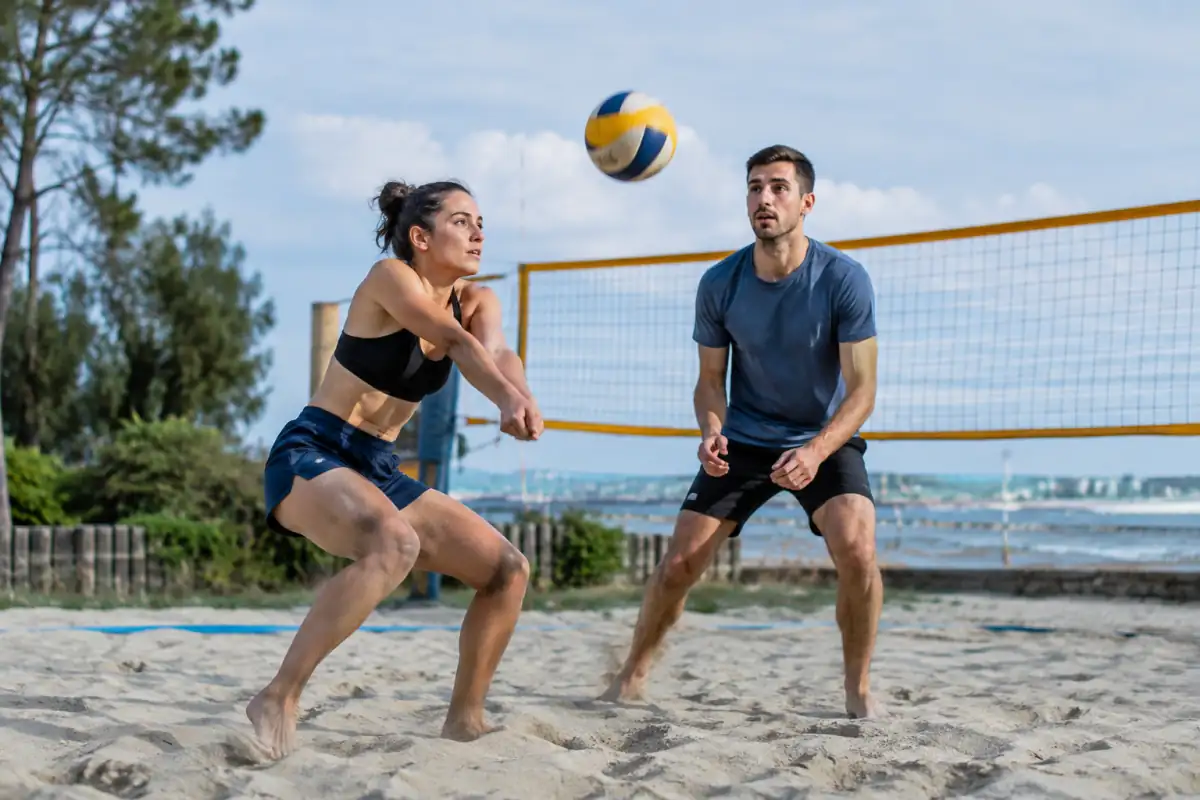 Deux joueurs réceptionnent un ballon et se replacent lors d’un échange de beach-volley sur un terrain de sable.