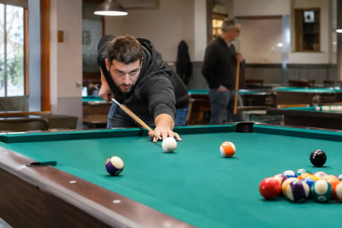 Joueur visant la bille blanche sur une table à six poches lors d’une partie de billard américain en salle.