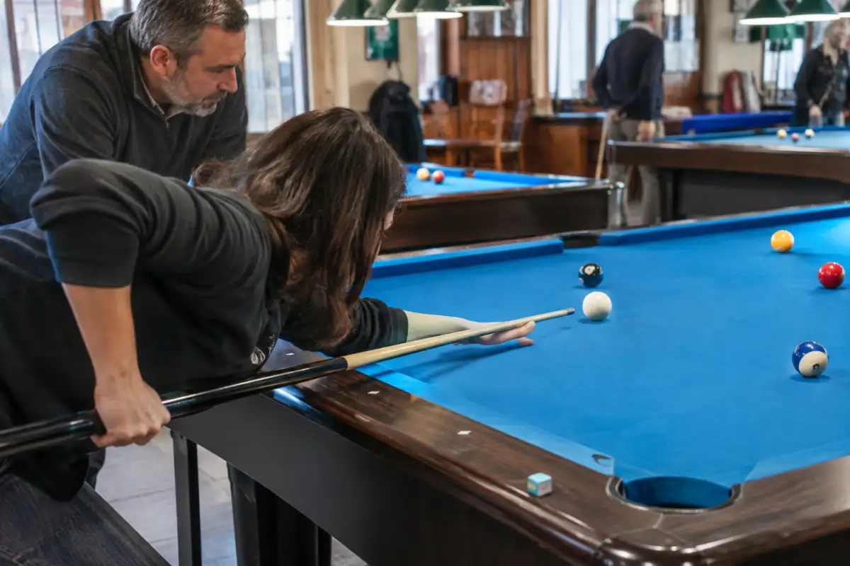 Débutant en club, en position pour un coup droit au billard américain, sous le regard attentif d’un encadrant.