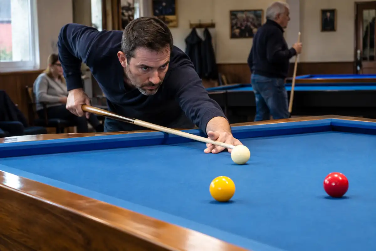 Une joueuse exécute une figure de billard artistique sur une table de carambole avec trois billes et une queue.
