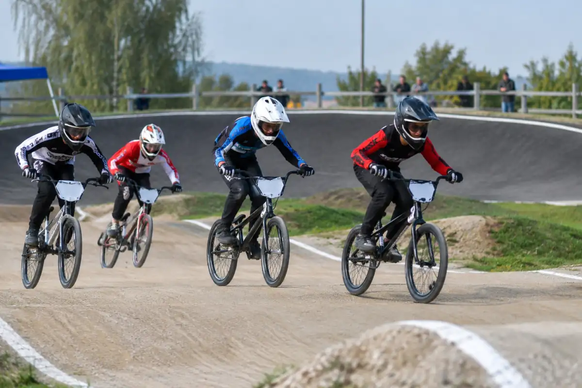 Des pilotes en casque intégral s’affrontent sur une piste de BMX racing avec bosses et virage relevé.