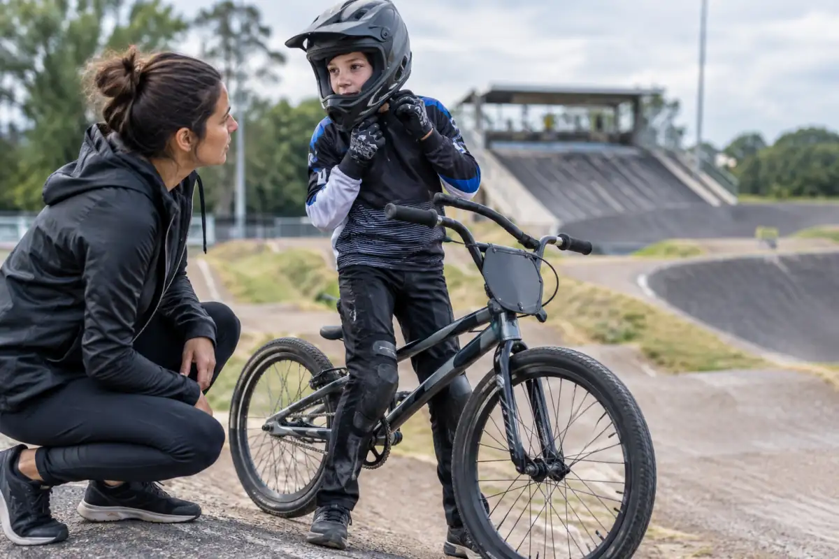 Débutant en BMX race ajustant son casque intégral près d’un vélo de course à sa taille, avec gants et protections adaptées à la piste.