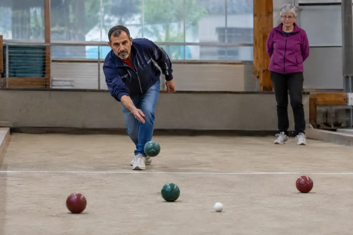 Un joueur lance une boule sur un terrain de bocce raffa tandis que le pallino et les autres boules sont visibles.