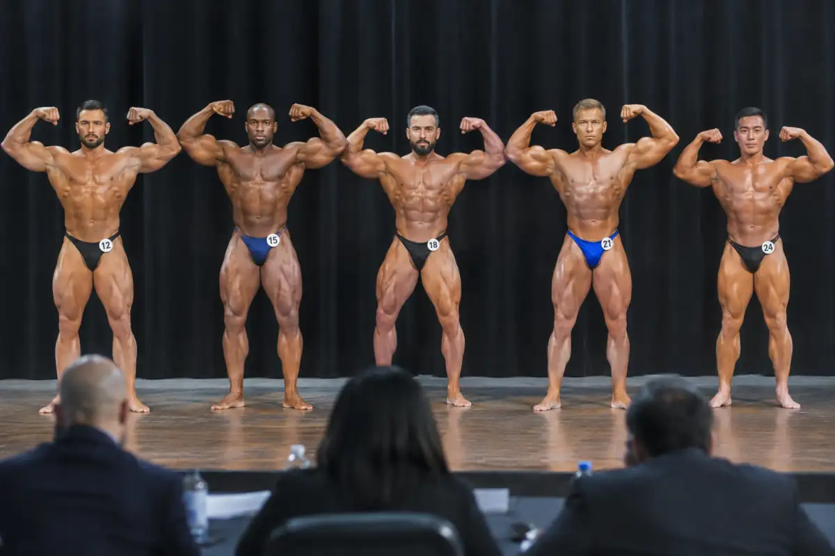 Athlètes de bodybuilding alignés sur scène lors d’une comparaison, exécutant une pose réglementaire devant le jury.