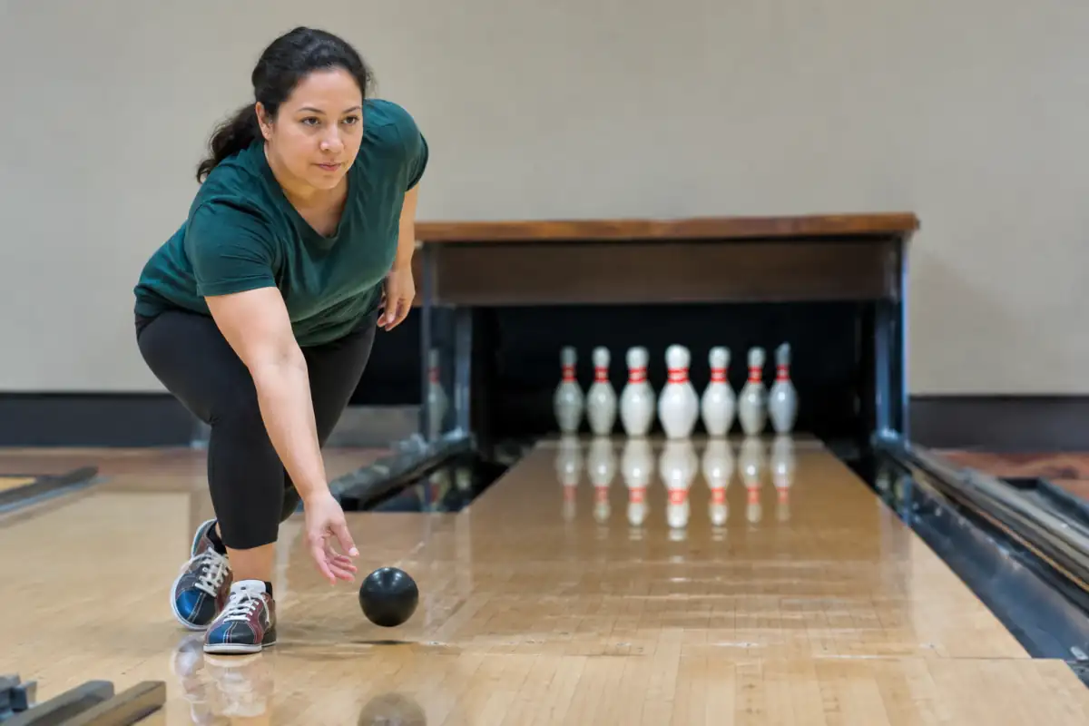 Un joueur lance une petite boule sans trous vers les quilles courtes sur une piste de bowling duckpin.