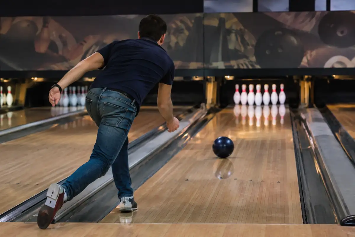 Joueur de bowling en fin de lancer, faisant rouler une boule vers les dix quilles alignées au fond de la piste.