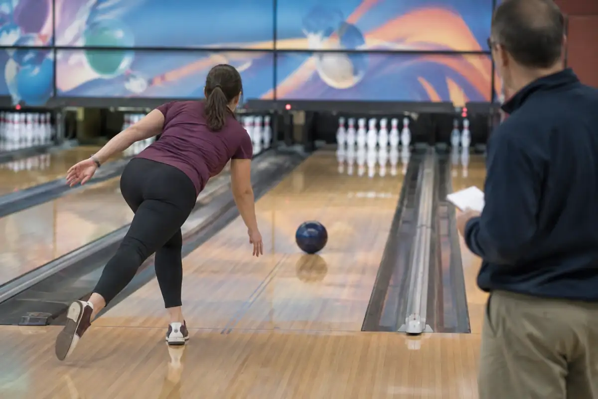 Joueur de bowling en position d’équilibre après son lancer, tandis qu’un entraîneur observe la régularité de son approche.
