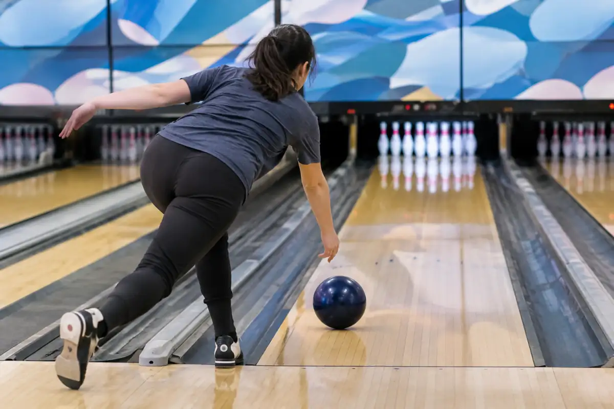 Débutant en glissade au bowling, lâchant la boule près de la cheville et visant les flèches de la piste.