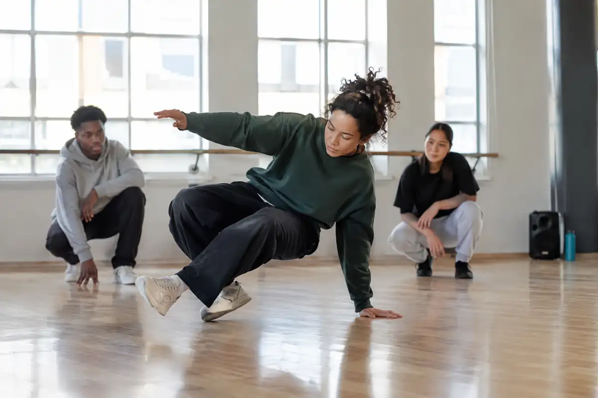 Une danseuse débutante travaille un déplacement de footwork contrôlé au sol dans une salle de breaking dégagée.