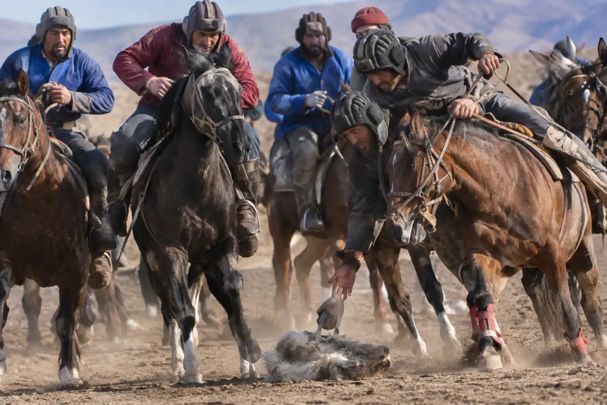 Cavaliers en tenue équestre se disputant une carcasse lors d’une partie de buzkashi sur un terrain extérieur.