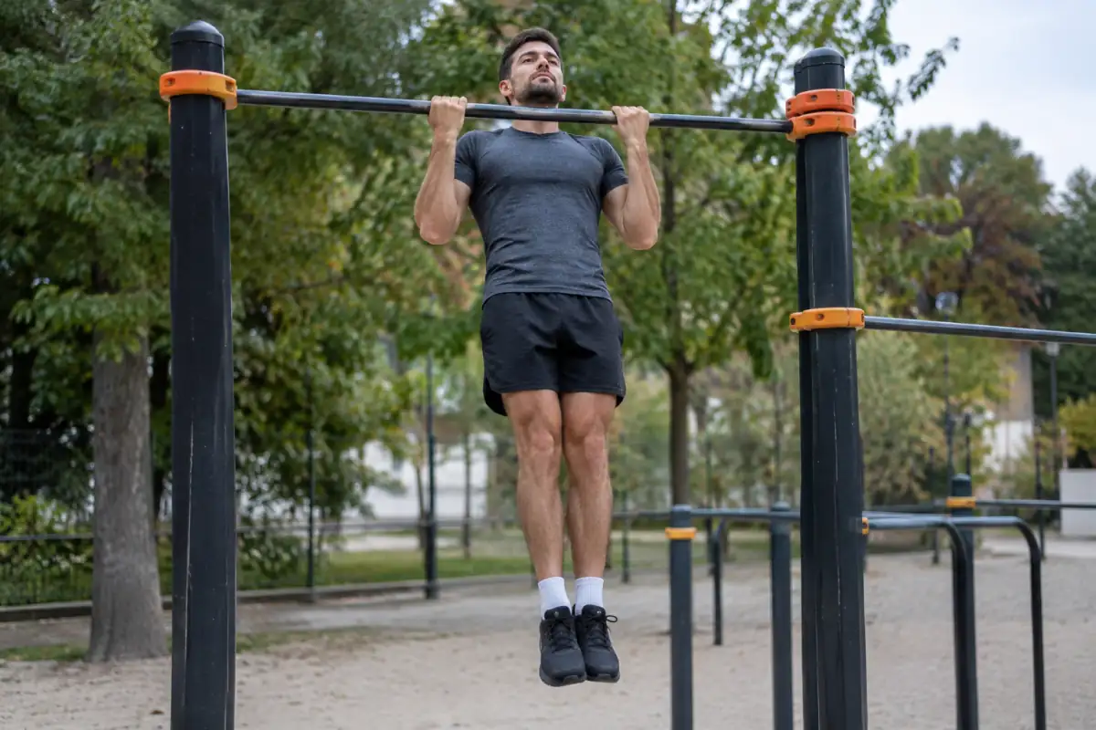 Une pratiquante de calisthenics réalise une traction contrôlée sur une barre dans un parc équipé.
