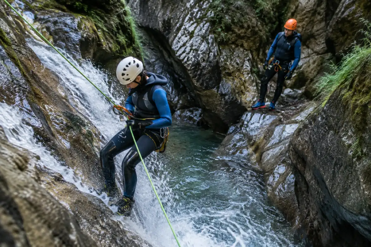 Deux pratiquants en combinaison et casque descendent un canyon français sur corde, sous la supervision d’un guide.