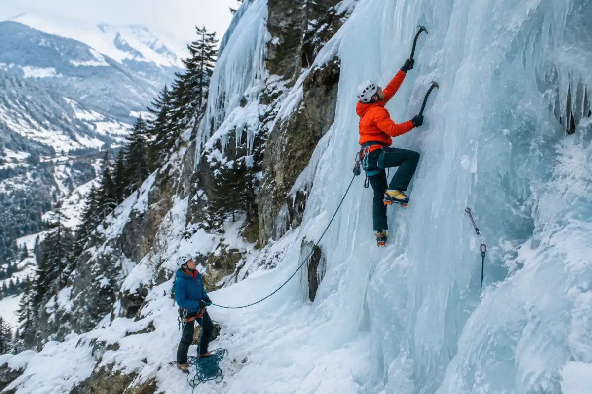 Deux grimpeurs encordés progressent sur une cascade de glace alpine avec piolets techniques, crampons, casques et vêtements d’hiver.