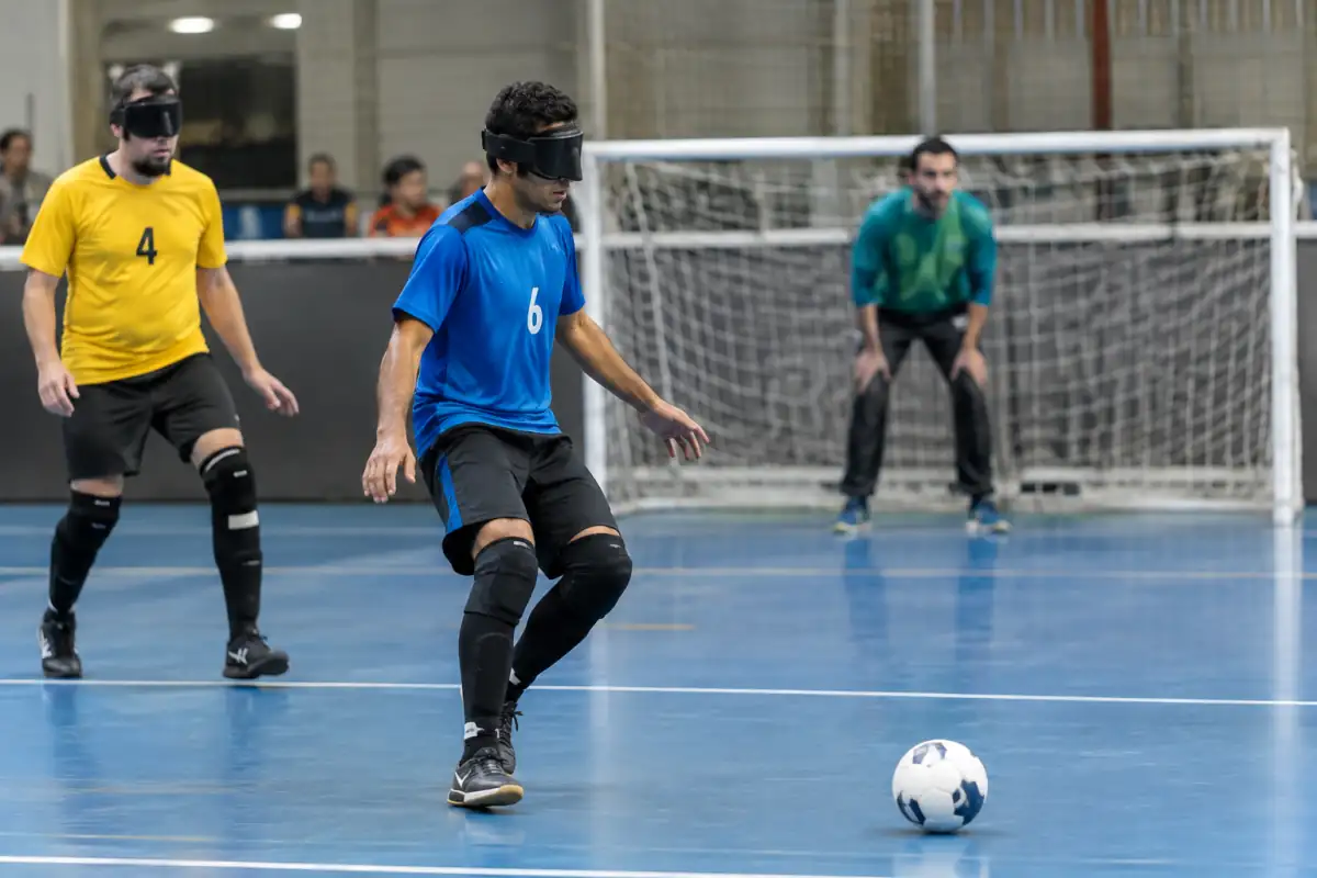 Un joueur de cécifoot B1 écoute le ballon sonore tandis que le guide l’oriente depuis l’arrière du but adverse.