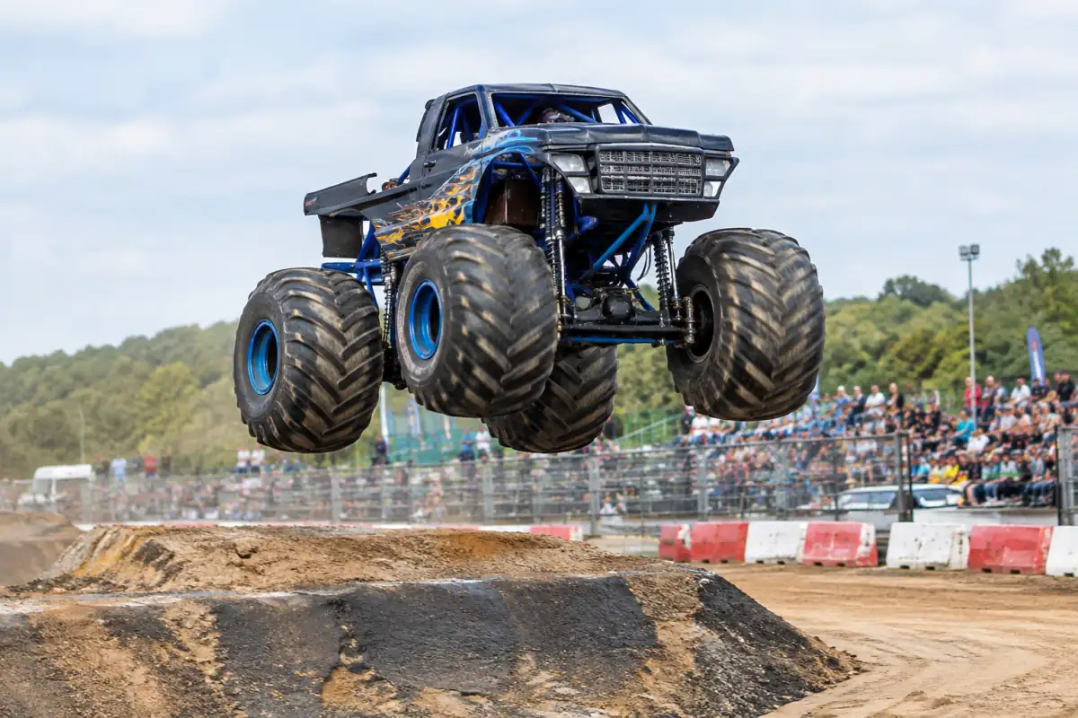 Un monster truck de compétition décolle d’une rampe en terre sur un circuit sécurisé, devant un public tenu à distance.