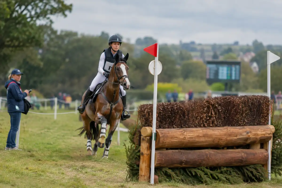 Un couple cavalier-cheval aborde un obstacle de cross balisé pendant une épreuve de concours complet, sous le regard d’un officiel.
