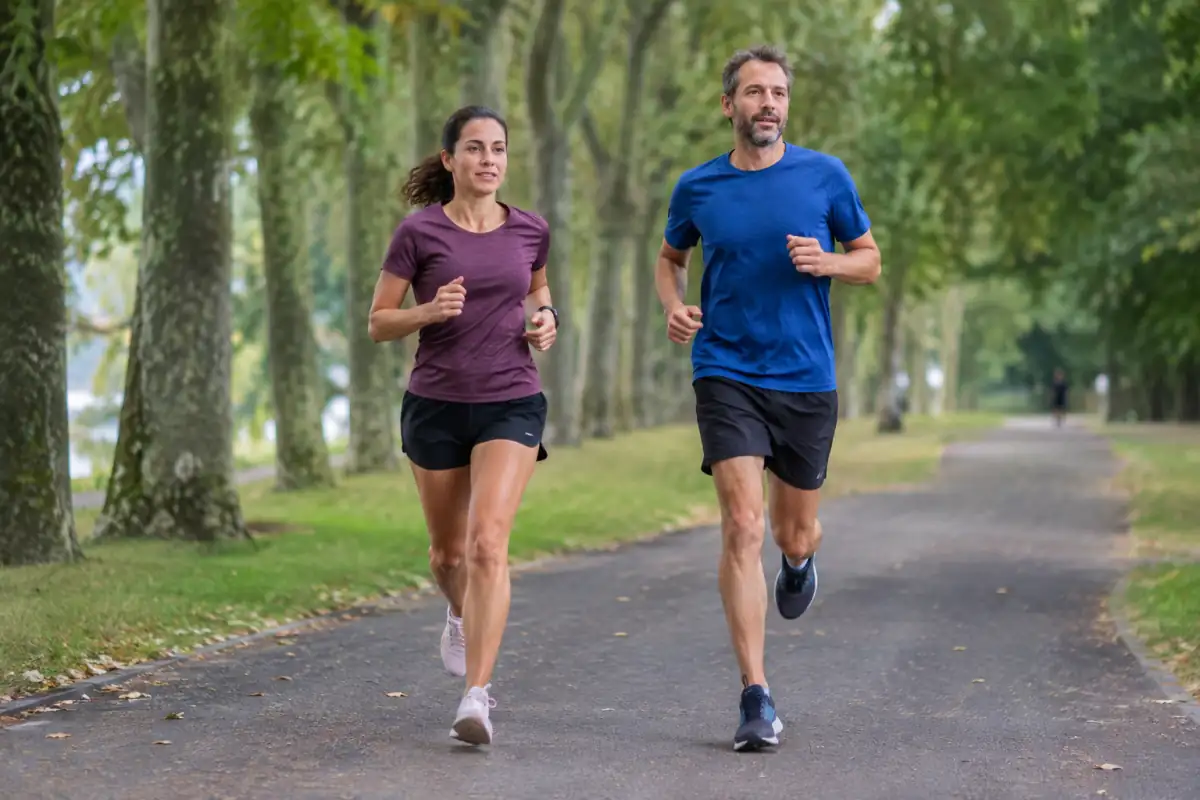 Deux coureurs amateurs avancent à allure tranquille sur une allée goudronnée bordée d’arbres lors d’une séance de course à pied.