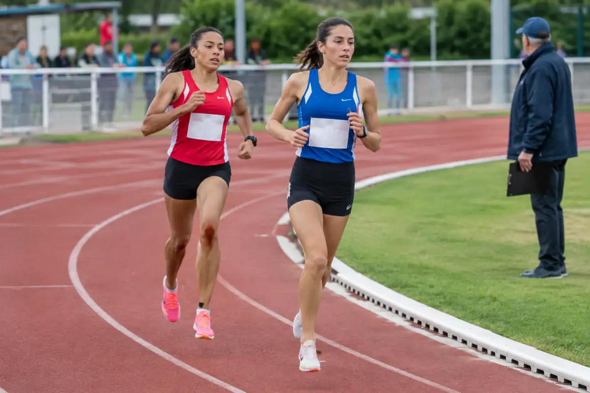 Deux coureurs se dépassent dans leurs couloirs sur une piste d’athlétisme, sous le regard d’un officiel.