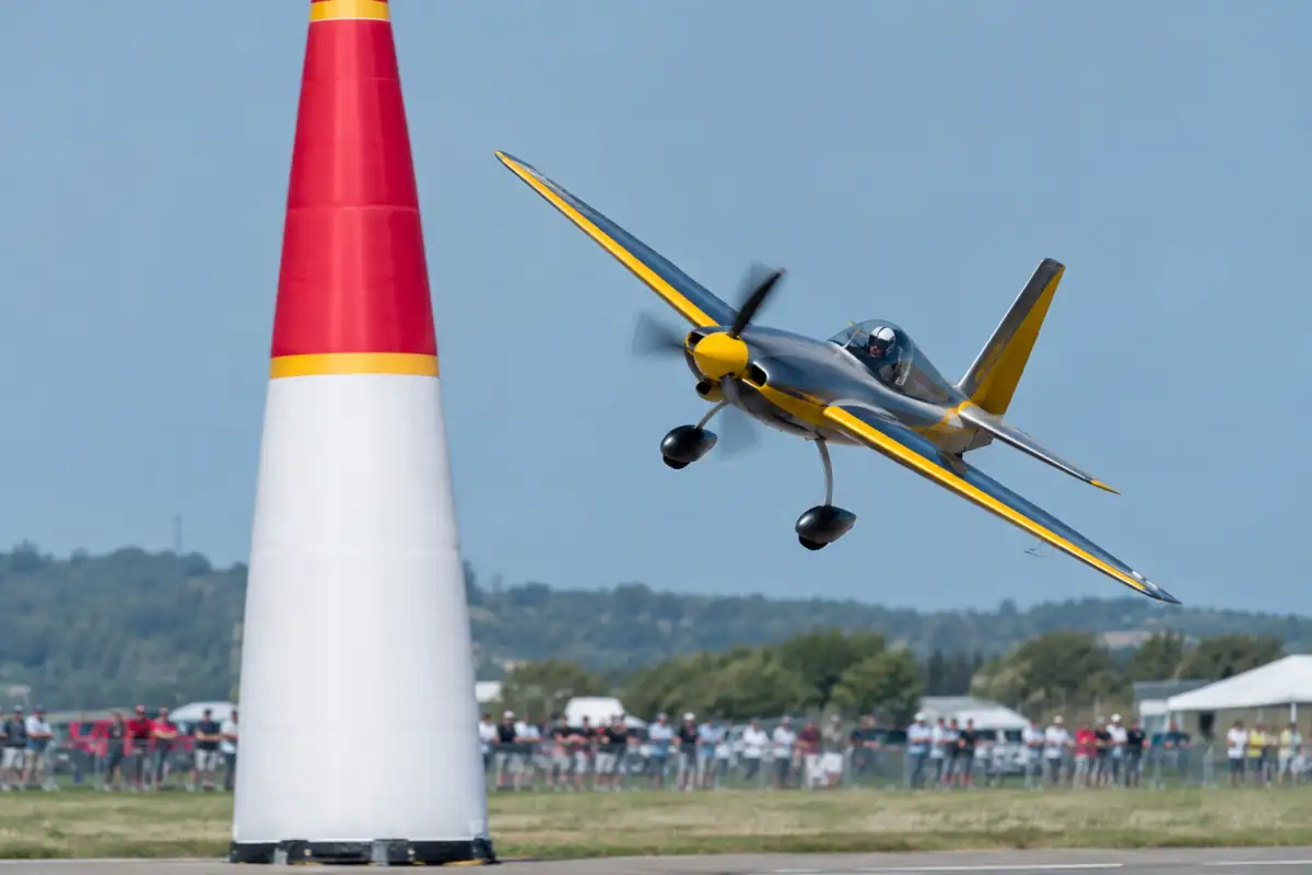 Un avion léger de course contourne un pylône sur un circuit aérien, piloté avec casque et équipement de vol.