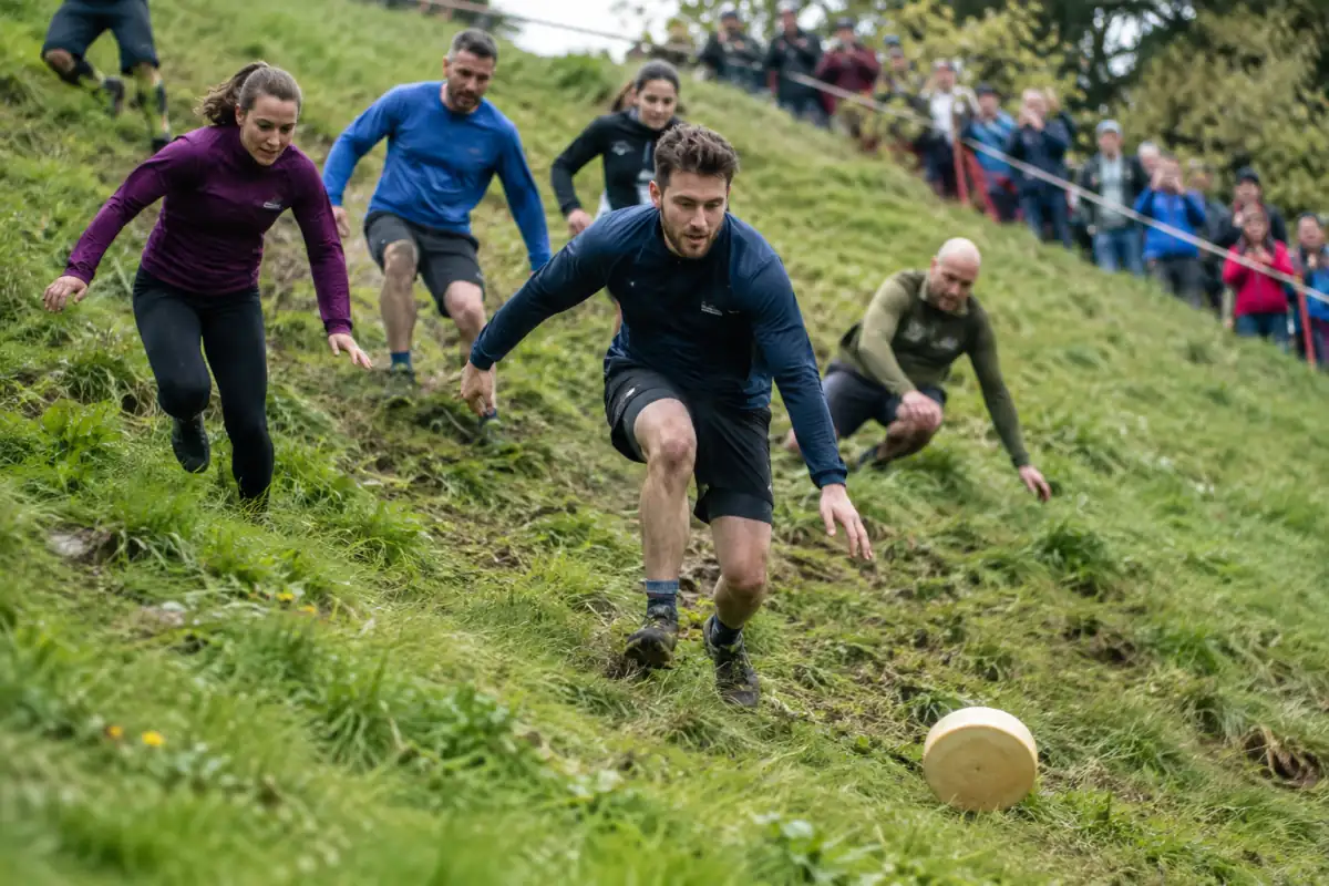 Course au fromage à Cooper’s Hill : des participants en tenue de course dévalent une pente herbeuse derrière une meule.