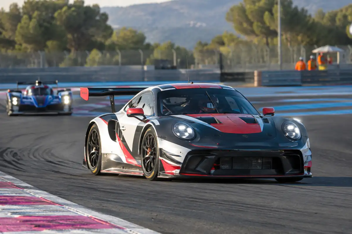 Voiture de course engagée en endurance automobile dans un virage de circuit, avec des pneus slicks et des barrières de sécurité.