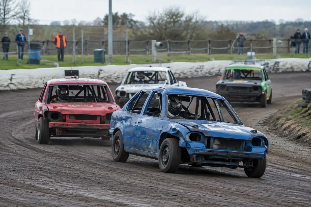 Une voiture de banger racing négocie un virage sur un ovale britannique, carrosserie marquée et arceau de sécurité visible.