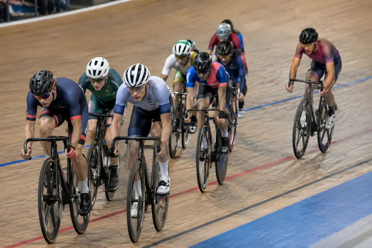 Coureurs en vélo à pignon fixe disputant un sprint intermédiaire d’une course aux points sur la piste inclinée d’un vélodrome couvert.
