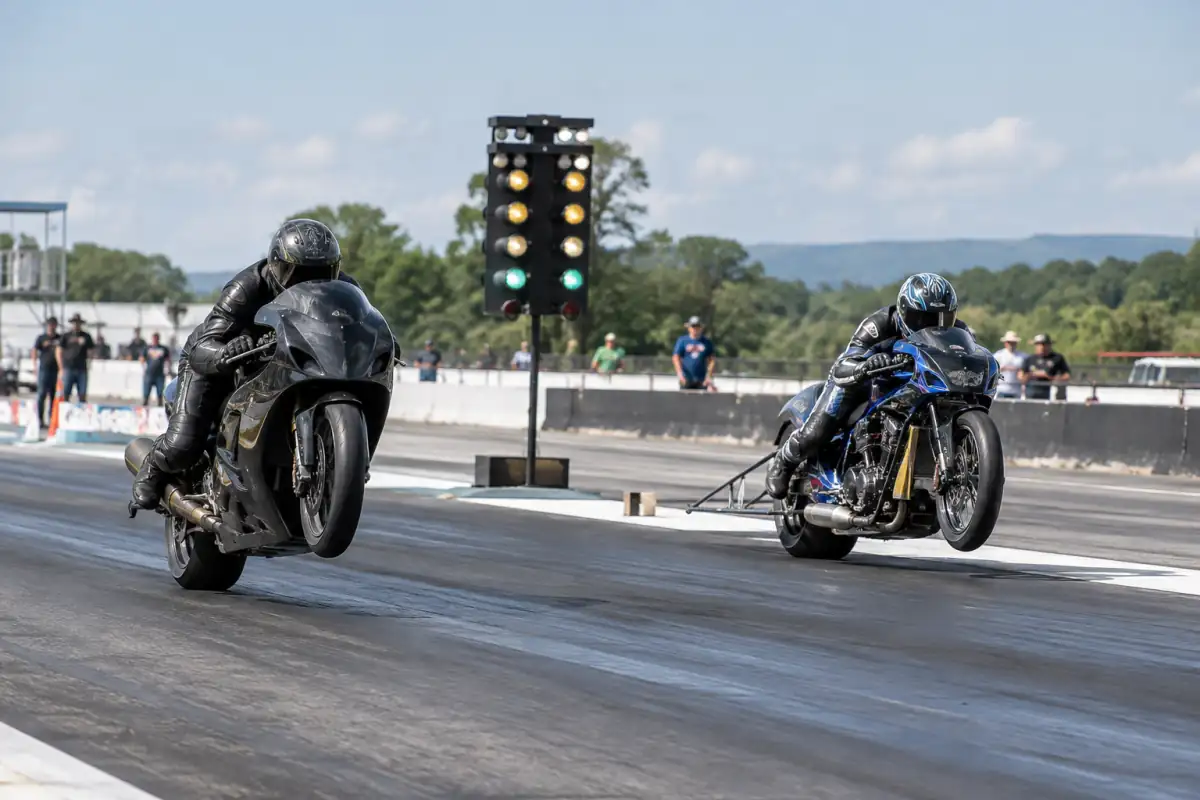 Deux pilotes en équipement intégral lancent leurs motos au feu sur une piste de course d’accélération moto.