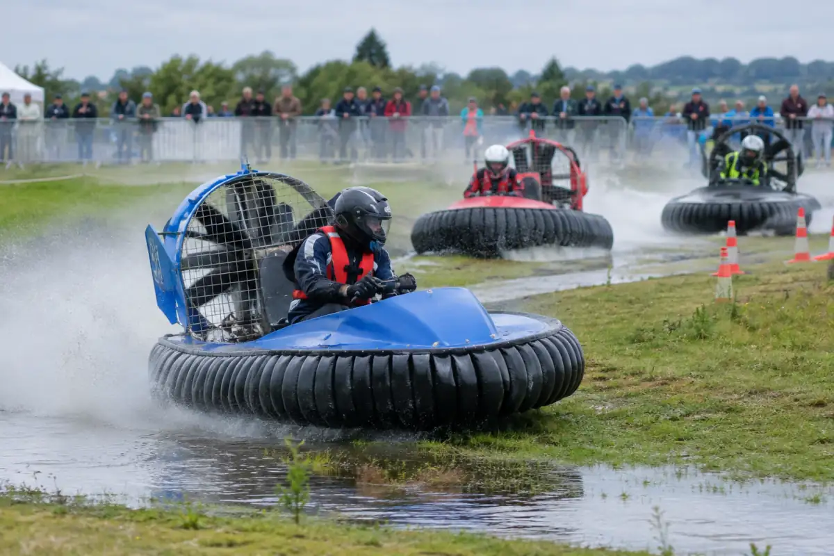 Course d’aéroglisseurs sur un parcours mêlant eau et herbe, avec des pilotes casqués dans leurs engins de compétition.