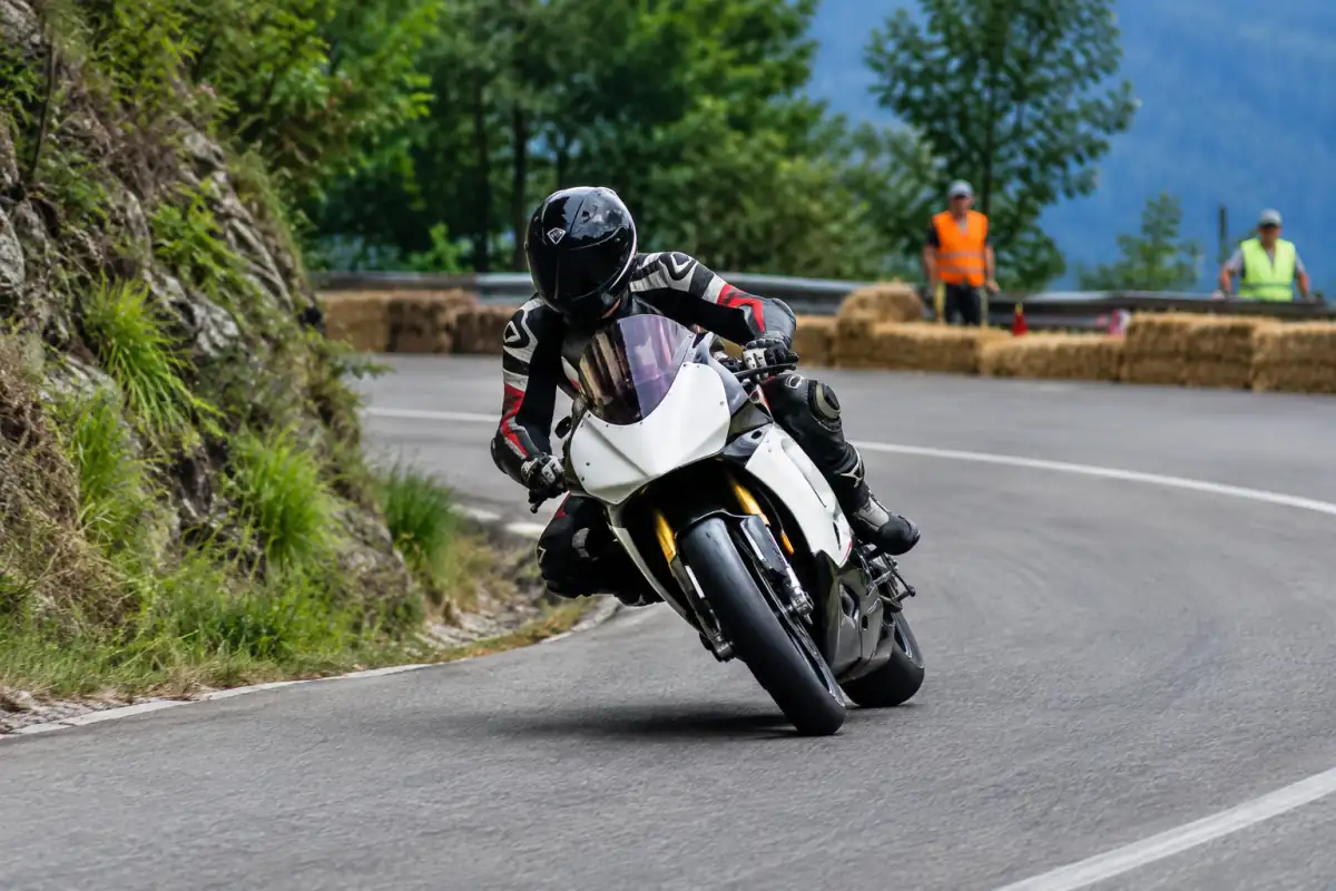 Pilote en combinaison et casque négocie un virage sur une route de montagne fermée lors d’une course de côte moto.