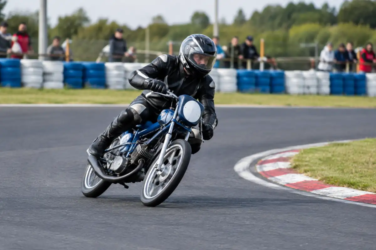 Pilote en combinaison et casque intégral négociant un virage sur un cyclomoteur préparé, lors d’une course sur circuit fermé.